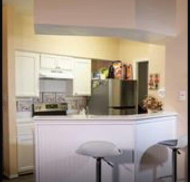 kitchen featuring range, extractor fan, white cabinets, and stainless steel refrigerator