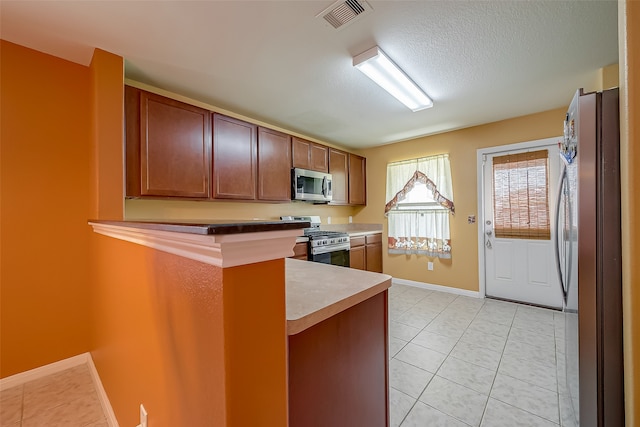 kitchen featuring stainless steel appliances, kitchen peninsula, light tile patterned floors, and a textured ceiling