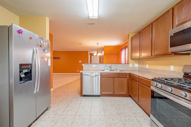 kitchen with appliances with stainless steel finishes, kitchen peninsula, pendant lighting, sink, and a notable chandelier