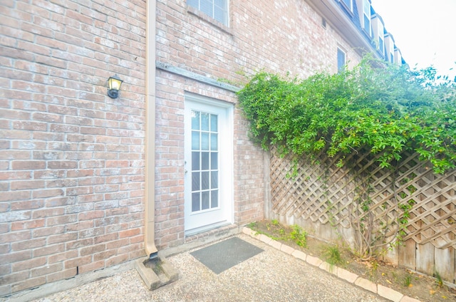 doorway to property featuring brick siding and fence