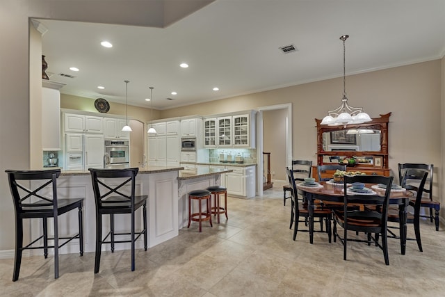 kitchen with light stone counters, backsplash, white cabinetry, built in appliances, and a kitchen breakfast bar