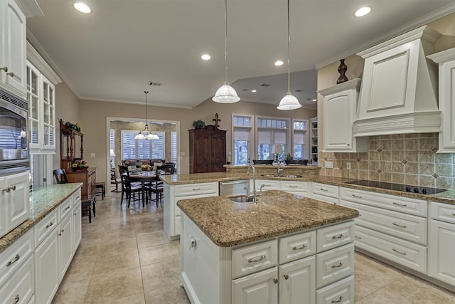 kitchen with white cabinetry, stainless steel appliances, decorative light fixtures, premium range hood, and a kitchen island with sink