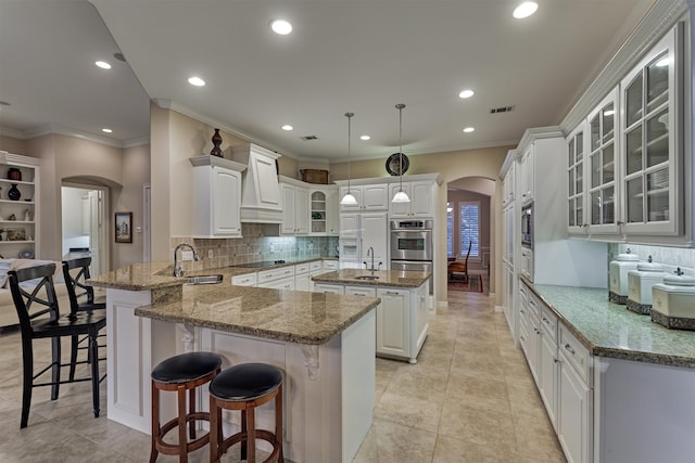 kitchen with sink, kitchen peninsula, a kitchen island, white cabinetry, and light stone countertops