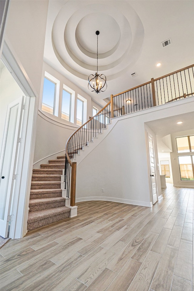 stairway featuring a high ceiling, a tray ceiling, hardwood / wood-style floors, and a chandelier