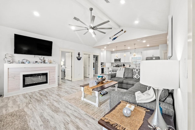 living room with ceiling fan, lofted ceiling with beams, and light wood-type flooring