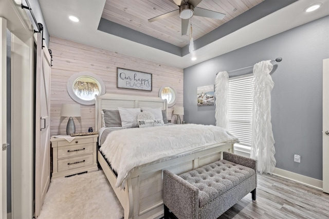 bedroom with wood ceiling, a tray ceiling, wooden walls, ceiling fan, and a barn door