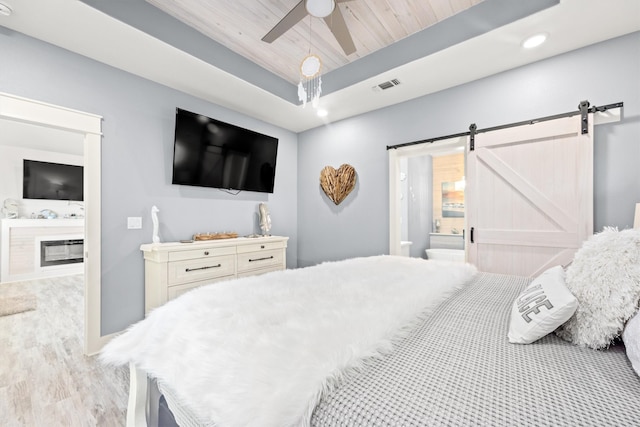 bedroom with wood ceiling, ensuite bath, a raised ceiling, ceiling fan, and a barn door