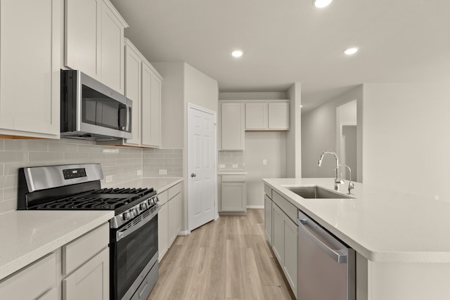 kitchen with stainless steel appliances, white cabinetry, light wood-type flooring, and sink