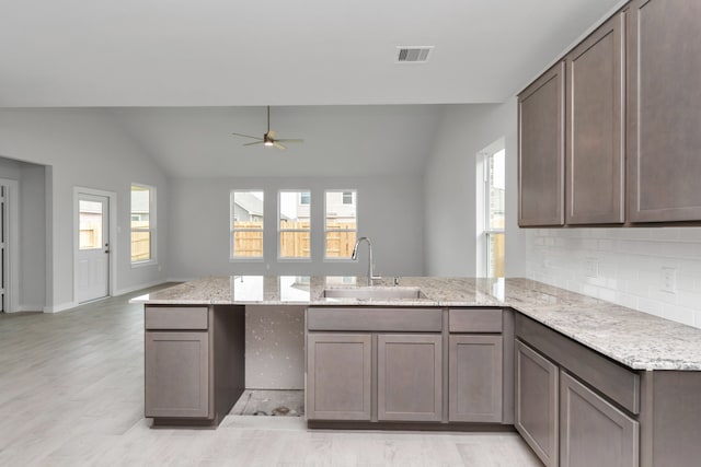 kitchen featuring ceiling fan, sink, kitchen peninsula, light hardwood / wood-style flooring, and vaulted ceiling