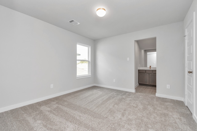 unfurnished bedroom featuring light colored carpet and ensuite bath