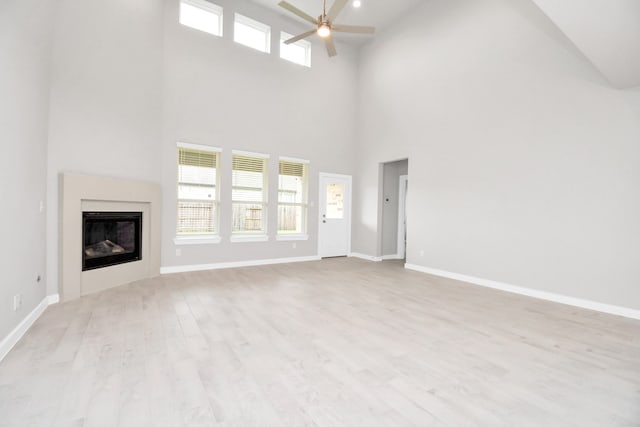 unfurnished living room featuring ceiling fan, light hardwood / wood-style flooring, and a towering ceiling