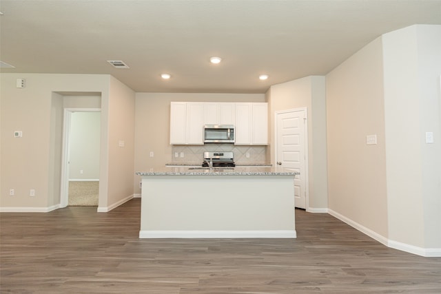 kitchen with appliances with stainless steel finishes, light stone counters, an island with sink, and white cabinets