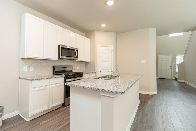 kitchen with appliances with stainless steel finishes, a center island with sink, sink, and white cabinets