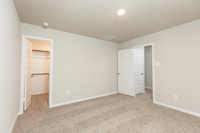 unfurnished bedroom featuring a spacious closet, a closet, light carpet, and a textured ceiling