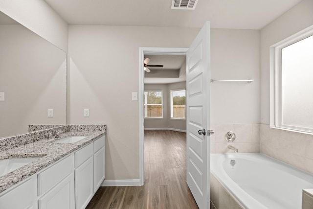 bathroom with hardwood / wood-style floors, vanity, a relaxing tiled tub, and ceiling fan