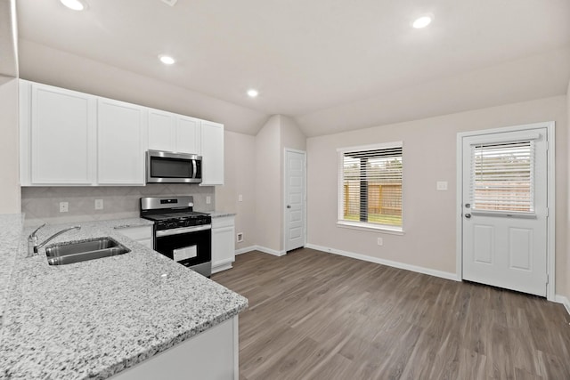 kitchen featuring light stone countertops, sink, vaulted ceiling, white cabinets, and appliances with stainless steel finishes