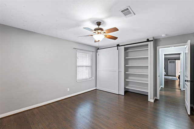 unfurnished bedroom featuring ceiling fan, a closet, dark wood-type flooring, and a barn door