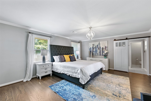 bedroom featuring dark wood-type flooring, a notable chandelier, a barn door, ensuite bath, and ornamental molding