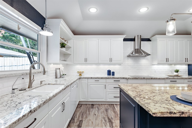 kitchen featuring white cabinetry, light wood-type flooring, decorative light fixtures, sink, and wall chimney range hood