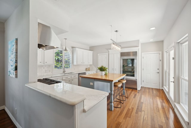 kitchen featuring white cabinets, kitchen peninsula, decorative light fixtures, a kitchen breakfast bar, and range hood