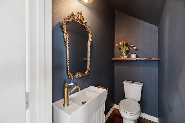 bathroom featuring wood-type flooring, vanity, lofted ceiling, and toilet