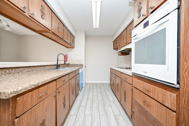 kitchen with sink, wall oven, stainless steel dishwasher, black electric stovetop, and light wood-type flooring