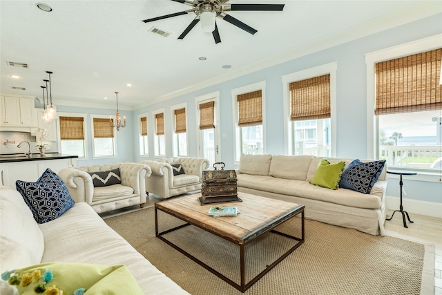 living area featuring ceiling fan with notable chandelier, baseboards, ornamental molding, and visible vents