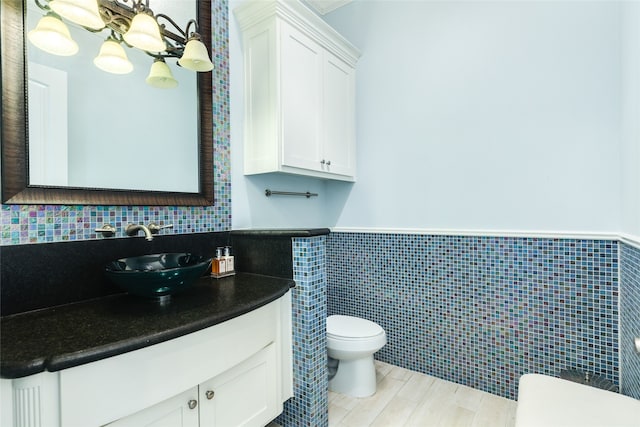 bathroom with an inviting chandelier, vanity, a wainscoted wall, toilet, and wood finished floors