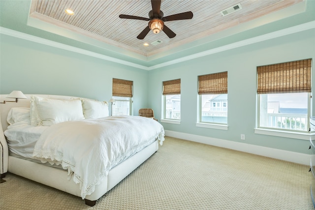 carpeted bedroom with ornamental molding, a tray ceiling, and multiple windows