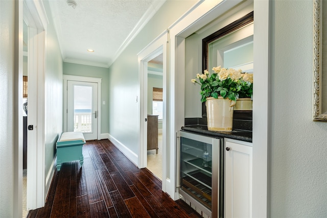 hallway with dark wood finished floors, a textured ceiling, ornamental molding, beverage cooler, and baseboards