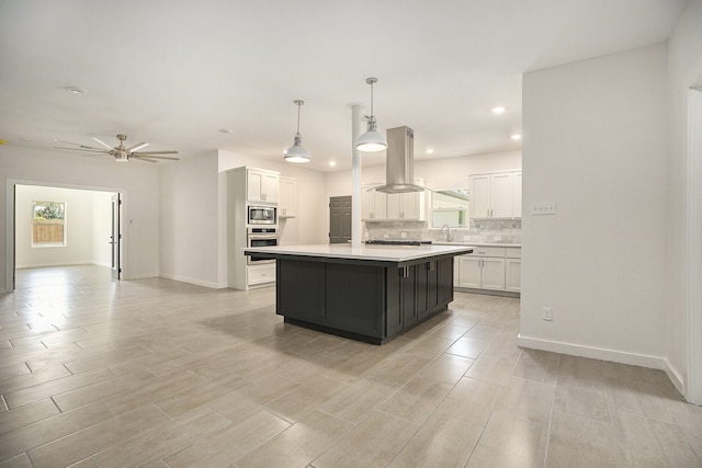 kitchen featuring hanging light fixtures, island range hood, a kitchen island, stainless steel appliances, and ceiling fan