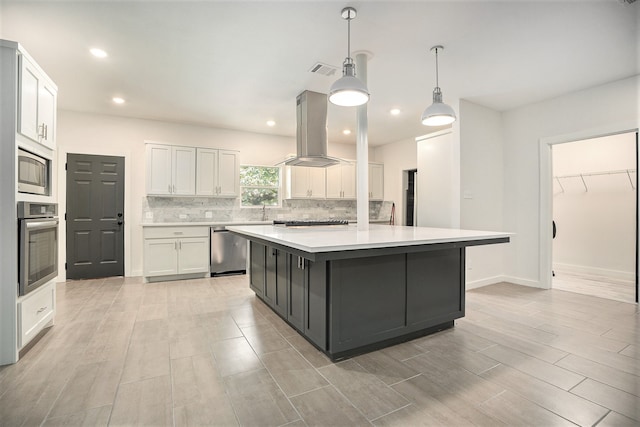 kitchen with white cabinets, hanging light fixtures, a kitchen island, island range hood, and appliances with stainless steel finishes