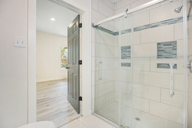 bathroom with wood-type flooring, a shower with shower door, and toilet