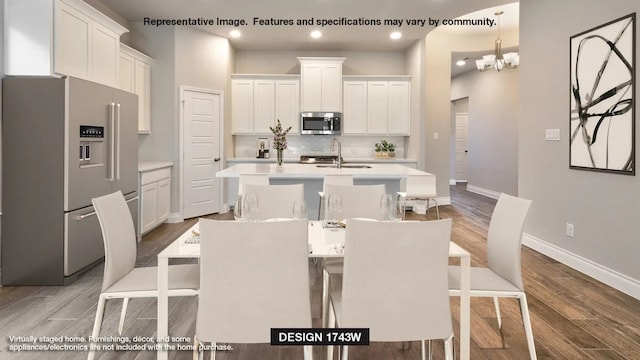 kitchen featuring a breakfast bar, hardwood / wood-style flooring, an island with sink, white cabinetry, and appliances with stainless steel finishes