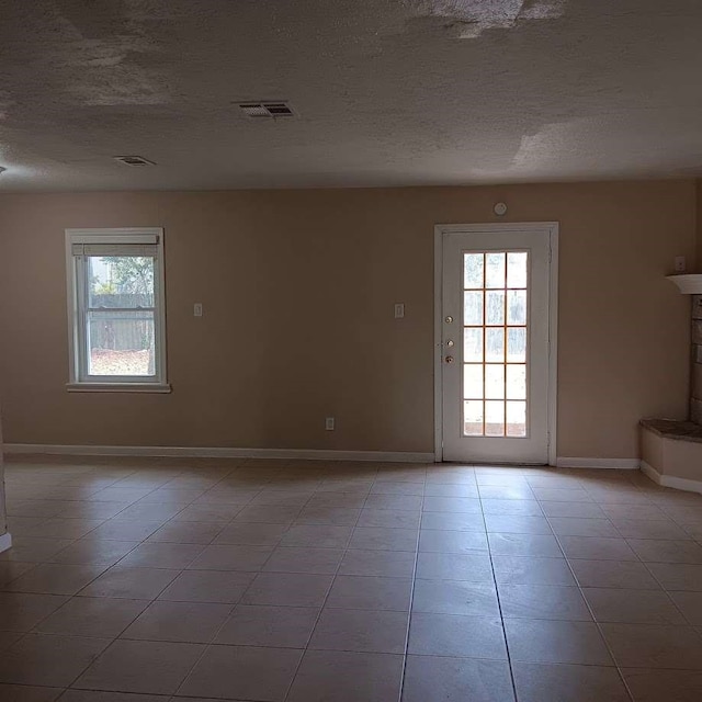 tiled empty room featuring a textured ceiling and plenty of natural light