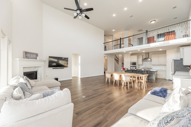 living room featuring ceiling fan, a towering ceiling, dark hardwood / wood-style flooring, and a tile fireplace