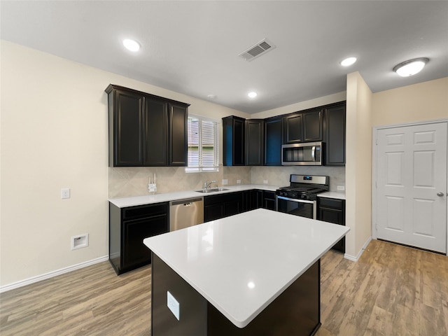 kitchen with appliances with stainless steel finishes, decorative backsplash, light wood-type flooring, a center island, and sink