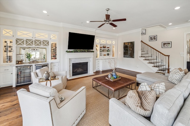 living room featuring ceiling fan, wine cooler, light hardwood / wood-style flooring, a fireplace, and crown molding