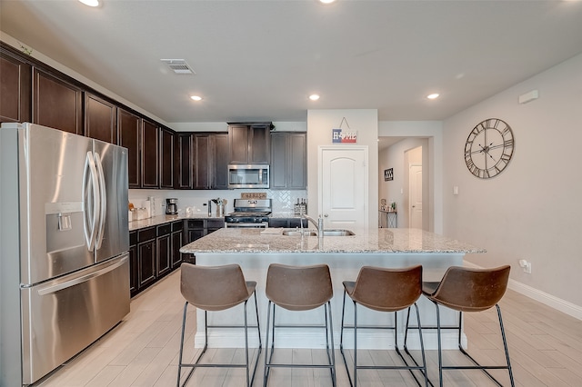 kitchen with appliances with stainless steel finishes, light stone countertops, sink, and an island with sink