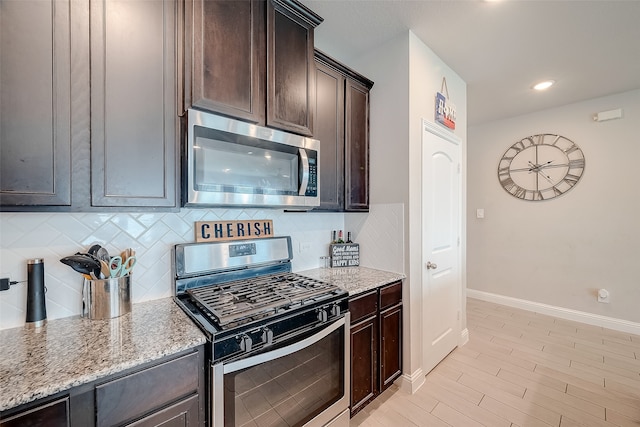 kitchen featuring dark brown cabinets, light stone counters, decorative backsplash, stainless steel appliances, and light hardwood / wood-style flooring