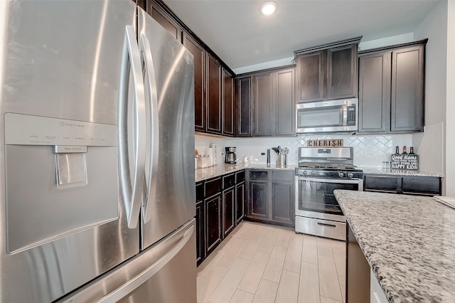 kitchen featuring dark brown cabinets, light stone countertops, stainless steel appliances, and backsplash