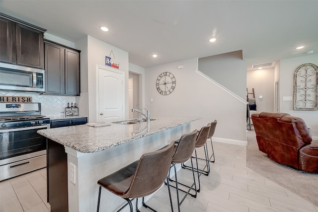 kitchen featuring a breakfast bar, light stone counters, sink, a center island with sink, and appliances with stainless steel finishes