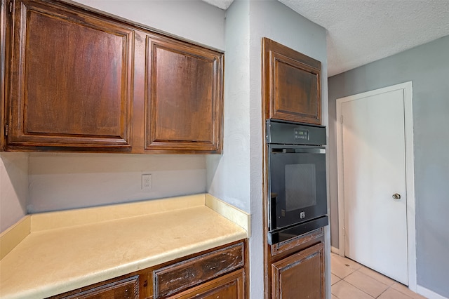 kitchen featuring black oven, a textured ceiling, and light tile patterned flooring