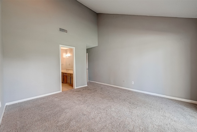 unfurnished bedroom with ensuite bath, light carpet, and high vaulted ceiling