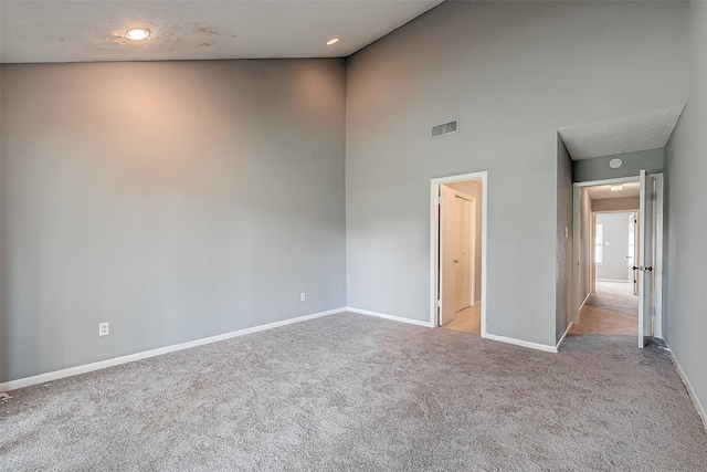 unfurnished bedroom with a textured ceiling, light carpet, and high vaulted ceiling