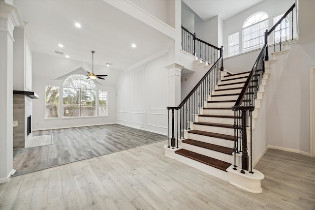 entrance foyer with light wood-type flooring, lofted ceiling, ceiling fan, decorative columns, and a premium fireplace