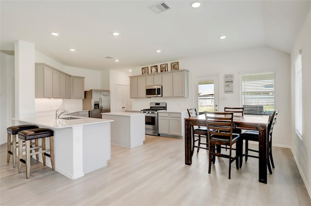 kitchen with gray cabinetry, stainless steel appliances, kitchen peninsula, a breakfast bar, and light wood-type flooring