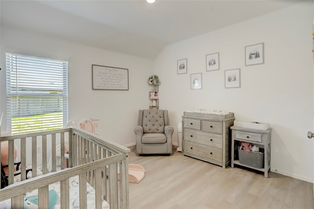 bedroom with light wood-type flooring, vaulted ceiling, and a nursery area