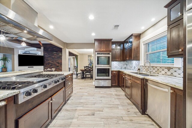 kitchen featuring sink, wall chimney exhaust hood, stainless steel appliances, light stone counters, and light hardwood / wood-style floors