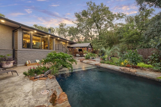 pool at dusk featuring a gazebo, a swimming pool, a patio area, and fence